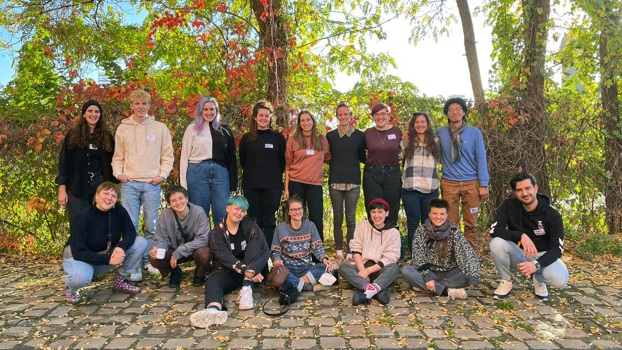 Gruppenfoto der Fachfortbildung Oktober 2022. Es sind 16 Teilnehmende, die in einem Wäldchen lächelnd in die Kamera gucken.