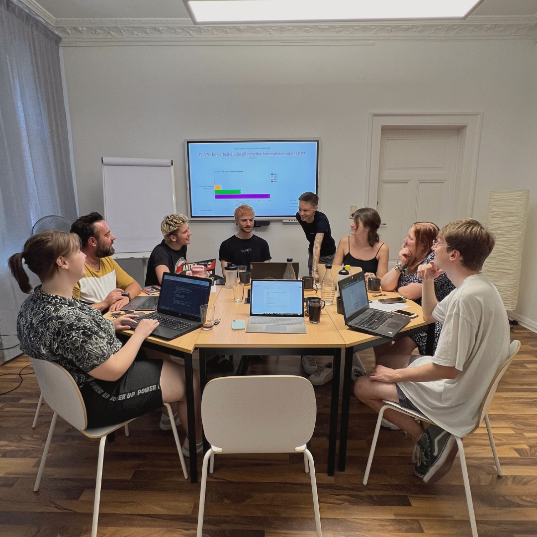 Acht Menschen aus der Planungsgruppe sitzen um einen runden Tisch und unterhalten sich.