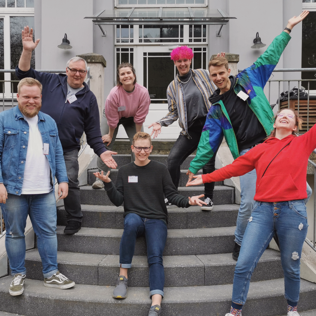 sieben Teilnehmende und Referierende der Grundqualifizierung stehen vor dem Waldschlösschen und lachen in die Kamera